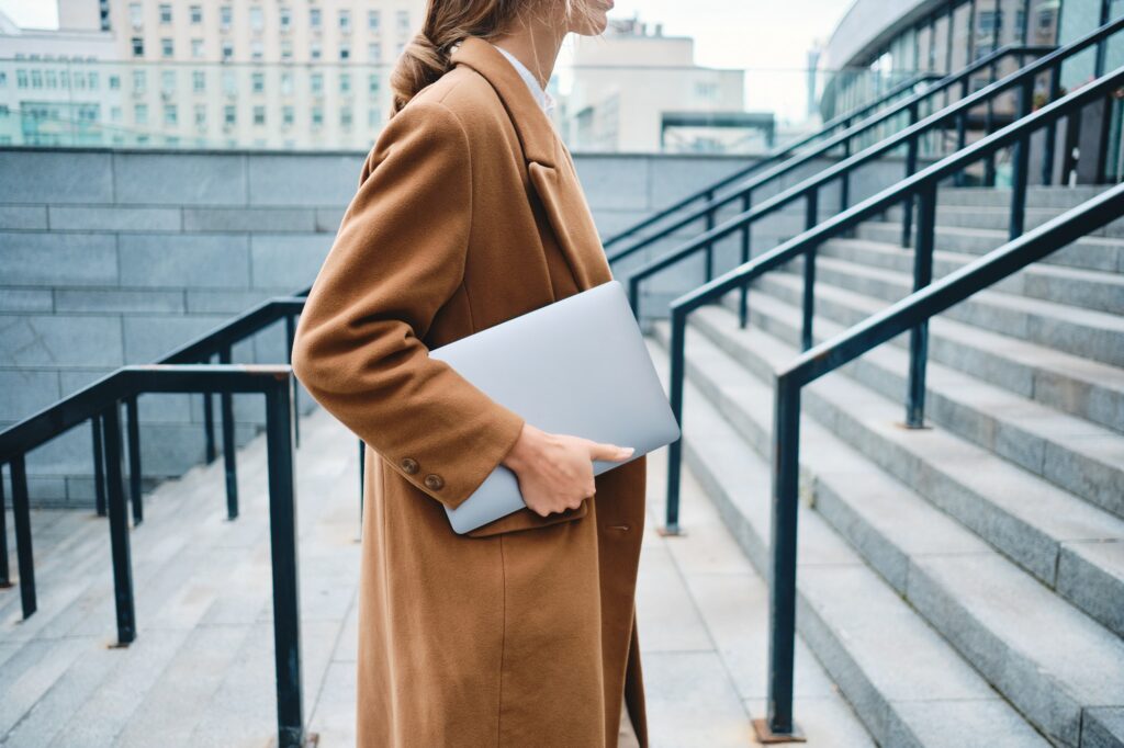 Close up stylish businesswoman in coat with laptop on city street